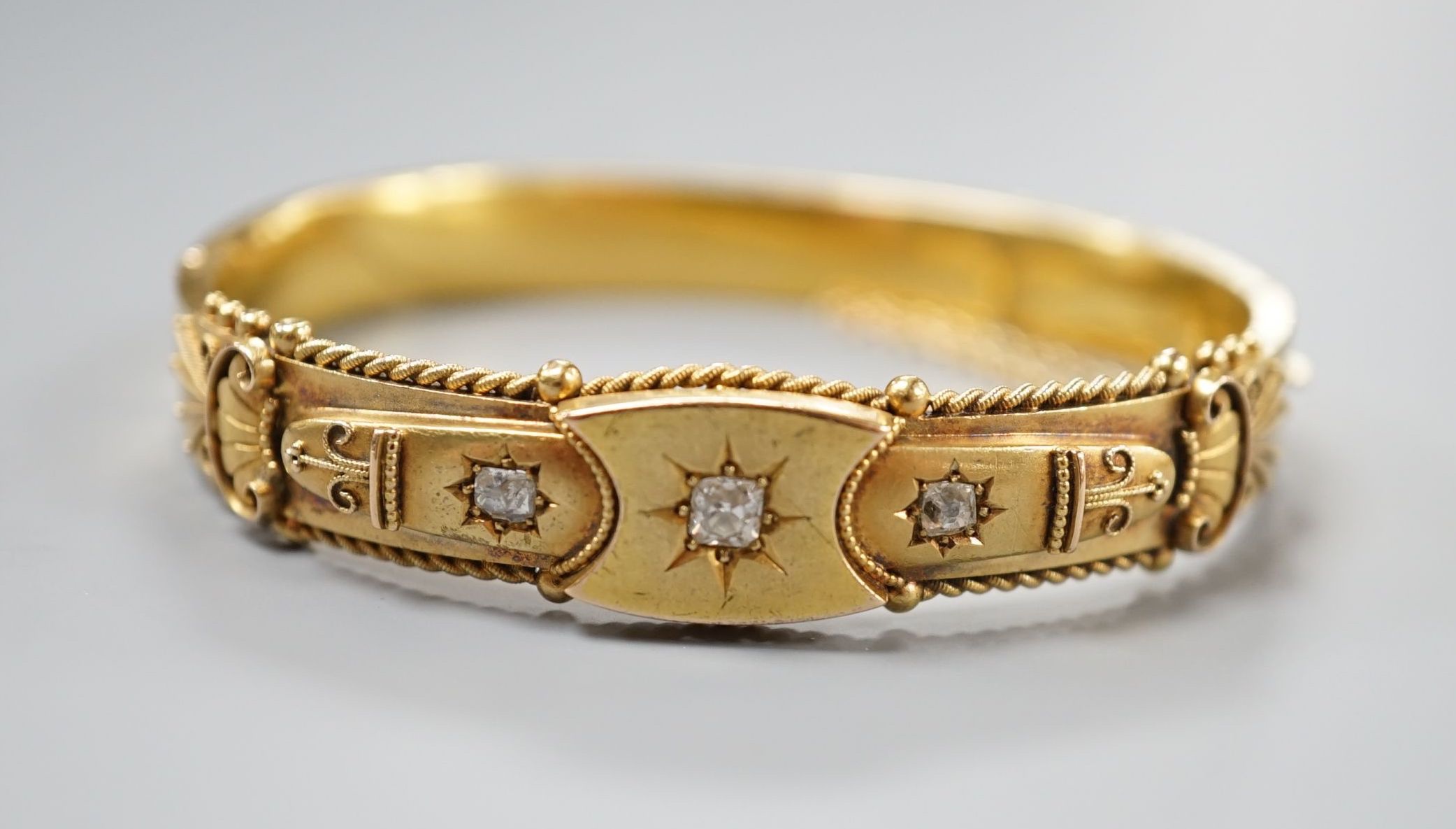An Edwardian 15ct gold and three stone diamond set hinged bangle, interior diameter 57mm, gross weight 15.8 grams.